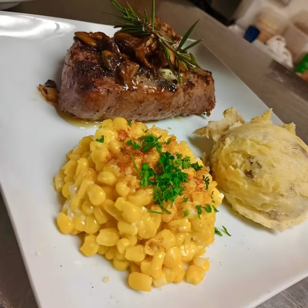 Water Tower Grille's steak with mushrooms, rosemary, creamed corn, and mashed potatoes on a white plate.