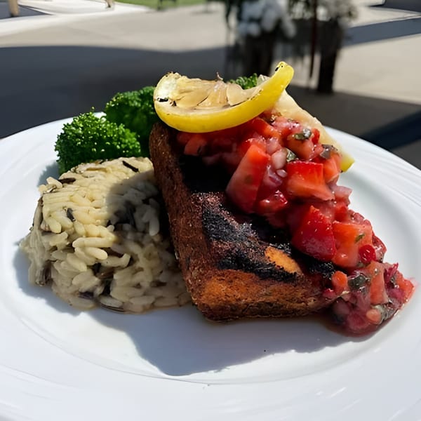 Grilled fish with tomato salsa, wild rice, and broccoli, garnished with a lemon wedge.