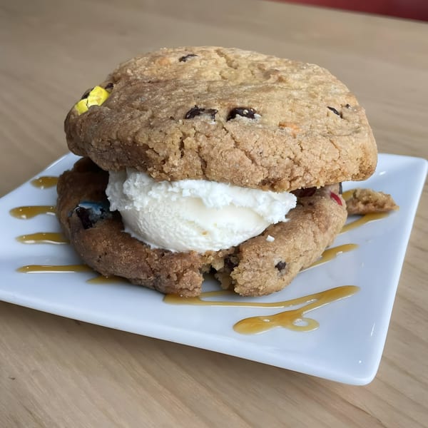 A large cookie sandwich with vanilla ice cream and caramel drizzle on a white plate.