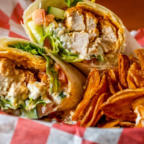 Two chicken wraps with lettuce, tomato, and sauce, served with crispy sweet potato fries.