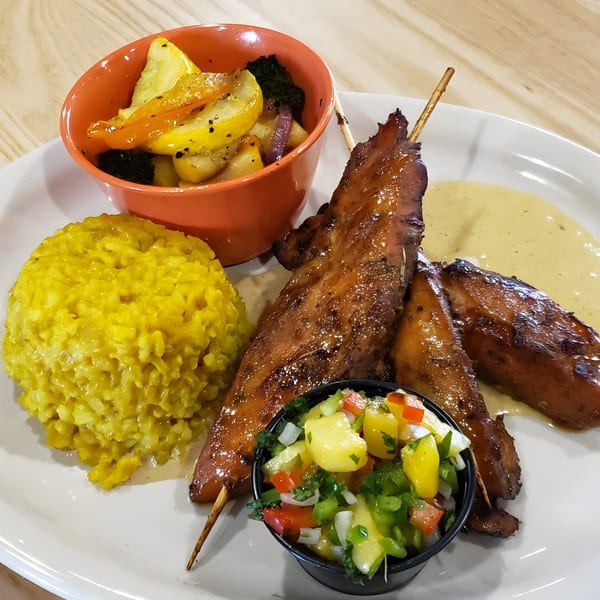 Grilled chicken skewers with yellow rice, roasted vegetables, and a side of mango salsa.
