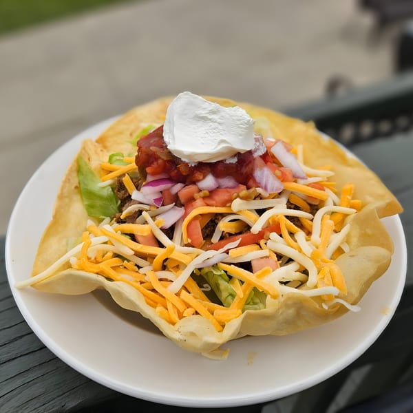 Taco salad in a crispy tortilla bowl, topped with ground beef, cheese, lettuce, salsa, and sour cream.